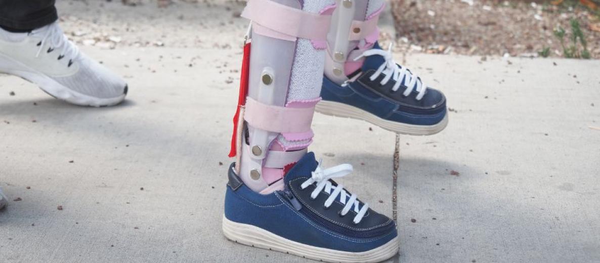 Zbliżenie na dziecięce nogi w ortezach i sportowych butach; logotyp ACE² i pasek logotypów uczelni.