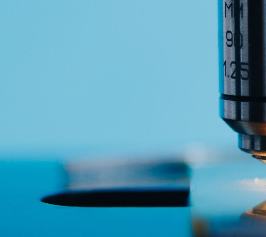Close-up of a microscope objective focusing light on a glass slide against a clean blue background.