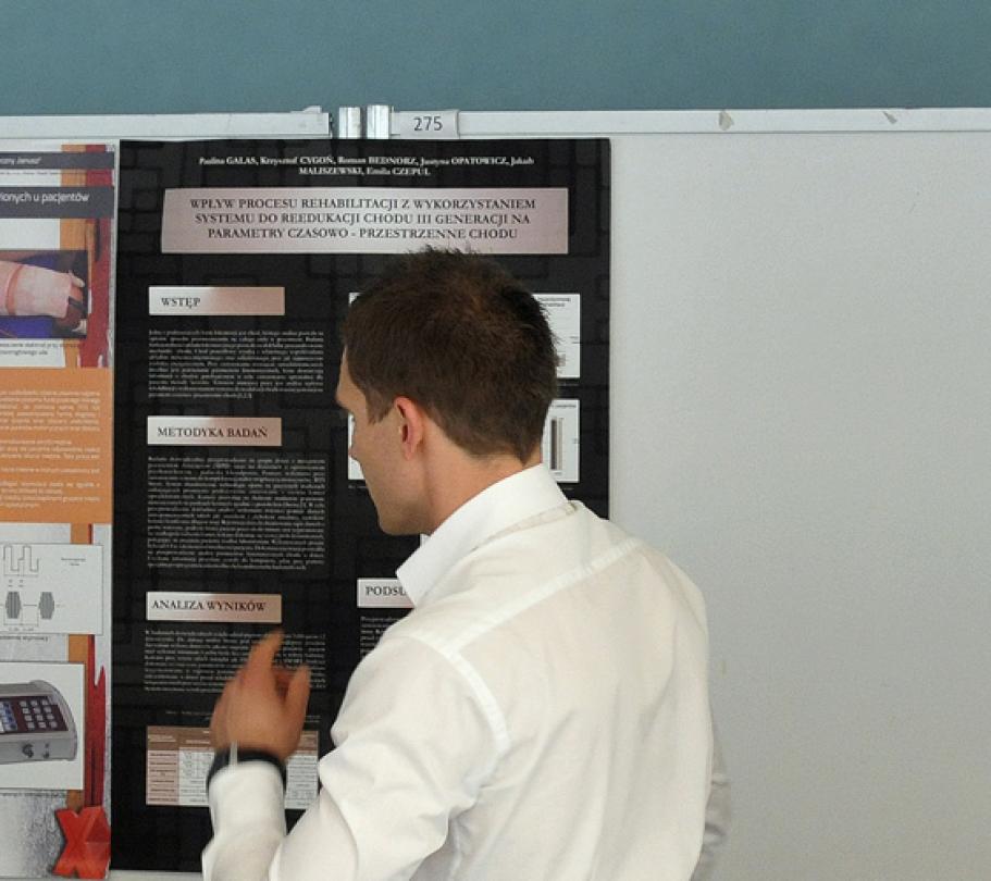 Studenci ze studenckiego towarzystwa naukowego omawiający plakat; odwróceni plecami do aparatu