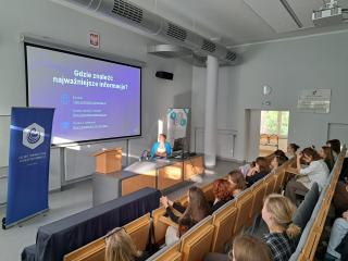 Wykład w auli; prowadząca przy pulpicie, na ekranie slajd „Gdzie znaleźć najważniejsze informacje?”, studenci na widowni.